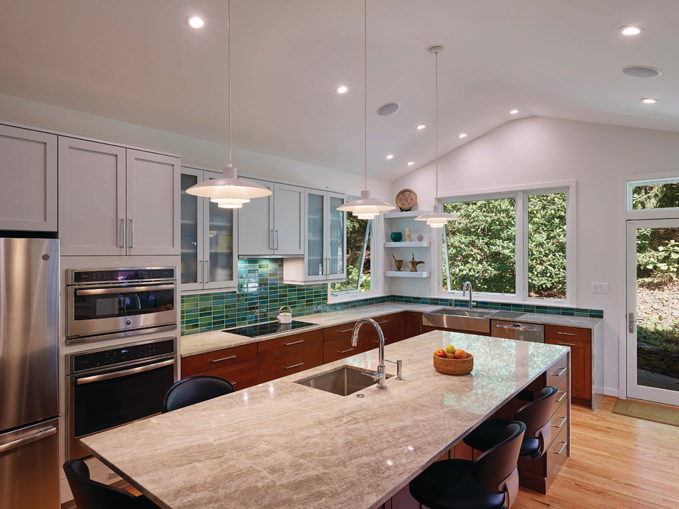 Foto på ett stort retro vit kök, med en undermonterad diskho, släta luckor, skåp i mellenmörkt trä, bänkskiva i kvarts, grönt stänkskydd, stänkskydd i porslinskakel, rostfria vitvaror, ljust trägolv, en köksö och brunt golv