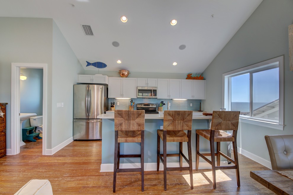 Design ideas for a medium sized coastal single-wall open plan kitchen in Tampa with shaker cabinets, white cabinets, composite countertops, blue splashback, ceramic splashback, stainless steel appliances, a belfast sink, bamboo flooring, an island and brown floors.