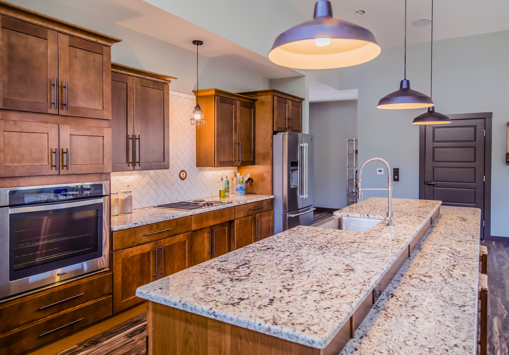 Example of a large transitional galley dark wood floor and brown floor open concept kitchen design in St Louis with a farmhouse sink, shaker cabinets, medium tone wood cabinets, granite countertops, white backsplash, stainless steel appliances, an island and ceramic backsplash