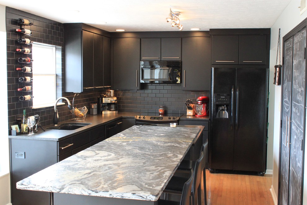 Modern inredning av ett mellanstort kök, med en undermonterad diskho, släta luckor, svarta skåp, granitbänkskiva, svart stänkskydd, stänkskydd i tunnelbanekakel, svarta vitvaror, mellanmörkt trägolv och en köksö
