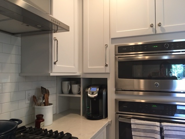 Photo of a large traditional l-shaped kitchen/diner in Indianapolis with a belfast sink, shaker cabinets, white cabinets, engineered stone countertops, white splashback, metro tiled splashback, stainless steel appliances, medium hardwood flooring and an island.