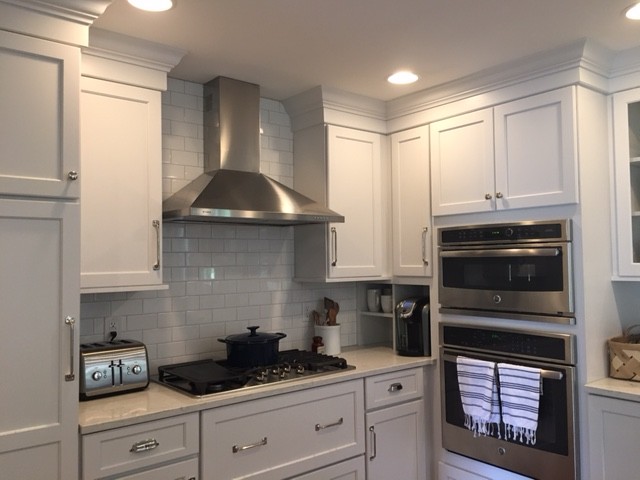 Large traditional l-shaped kitchen/diner in Indianapolis with a belfast sink, shaker cabinets, white cabinets, engineered stone countertops, white splashback, metro tiled splashback, stainless steel appliances, medium hardwood flooring and an island.