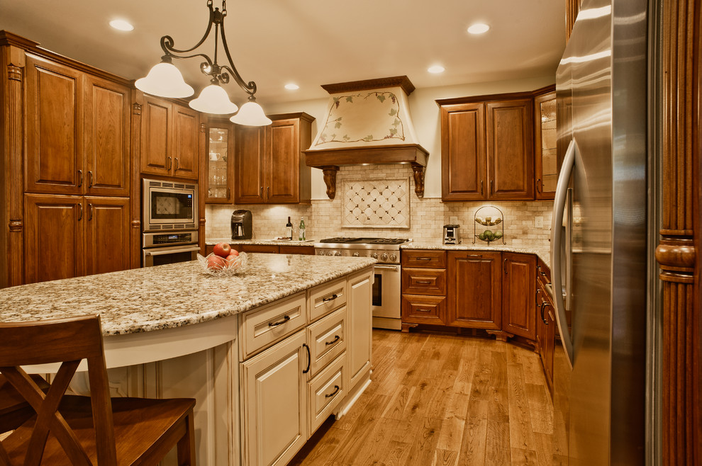Eat-in kitchen - traditional eat-in kitchen idea in Indianapolis with an undermount sink, raised-panel cabinets, brown cabinets, granite countertops, beige backsplash, stone tile backsplash and stainless steel appliances