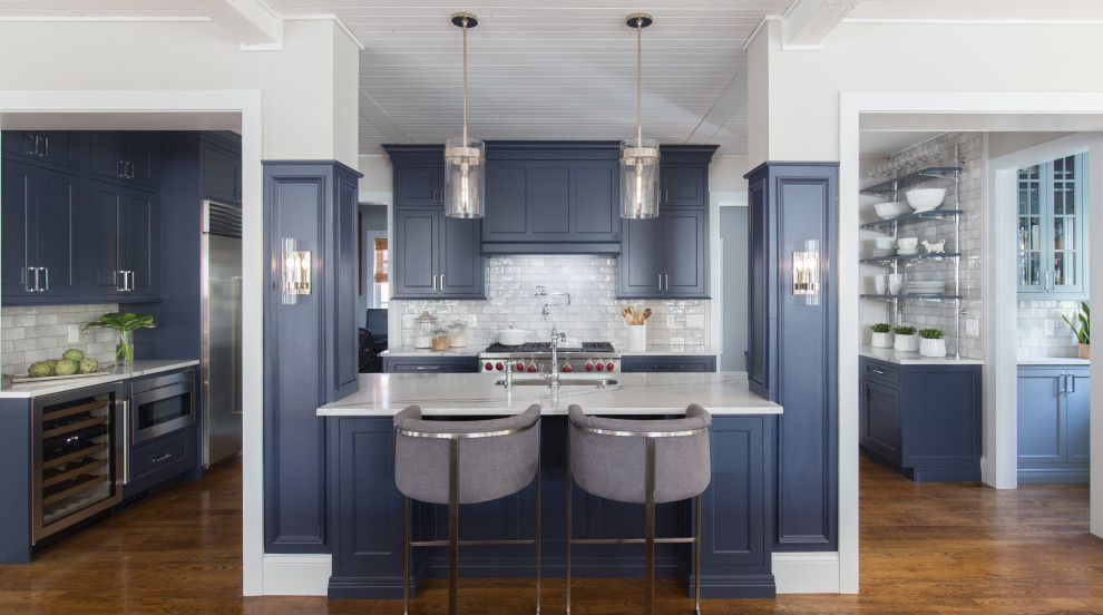 Inspiration for a medium sized traditional u-shaped open plan kitchen in St Louis with a submerged sink, flat-panel cabinets, blue cabinets, engineered stone countertops, grey splashback, ceramic splashback, integrated appliances, medium hardwood flooring, an island, brown floors and white worktops.