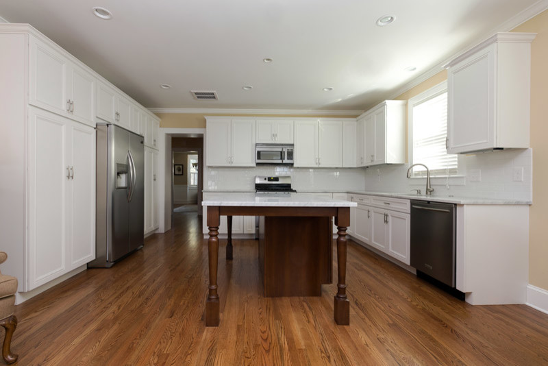 Large trendy u-shaped light wood floor and brown floor eat-in kitchen photo in Charleston with a drop-in sink, recessed-panel cabinets, white cabinets, marble countertops, white backsplash, subway tile backsplash, stainless steel appliances and an island