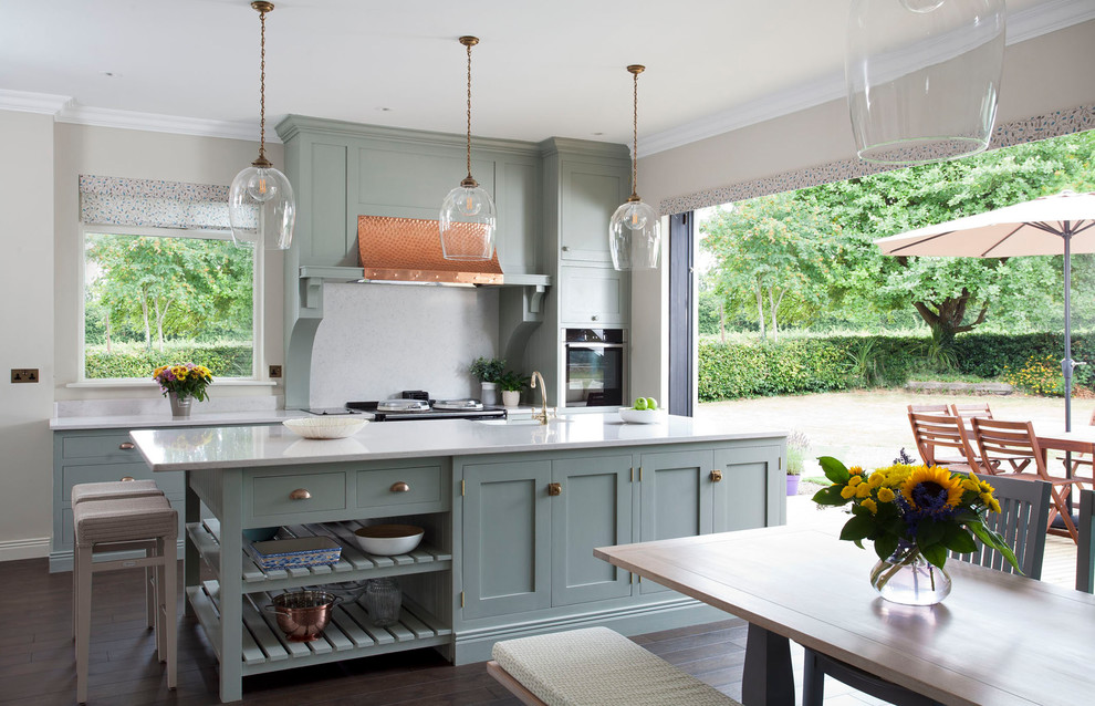 Zweizeilige Landhaus Wohnküche mit Schrankfronten im Shaker-Stil, blauen Schränken, Küchenrückwand in Grau, schwarzen Elektrogeräten, dunklem Holzboden, Kücheninsel, braunem Boden und weißer Arbeitsplatte in Hampshire