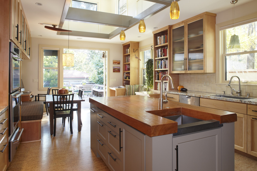 Example of a mid-sized minimalist l-shaped medium tone wood floor eat-in kitchen design in San Francisco with stainless steel appliances, an undermount sink, shaker cabinets, medium tone wood cabinets, granite countertops, beige backsplash, cement tile backsplash and an island