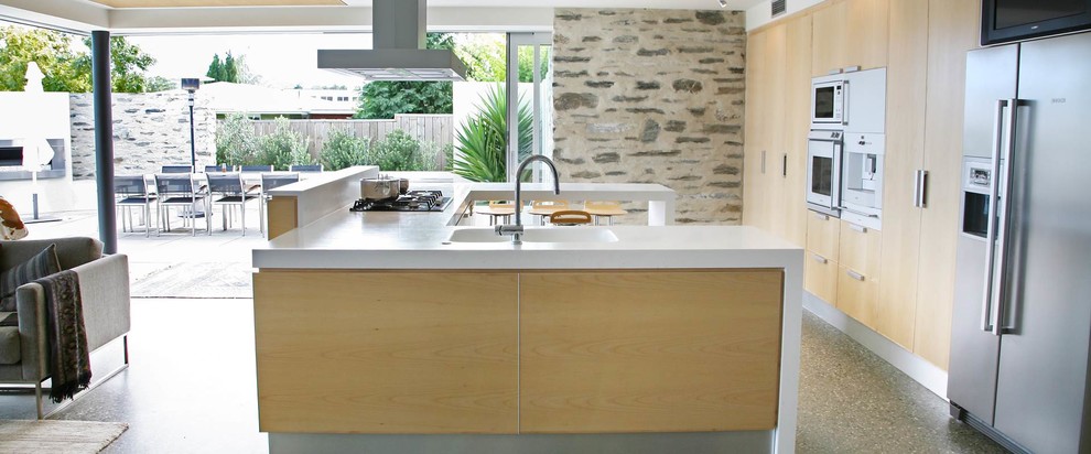 Immagine di una cucina moderna con lavello integrato, ante lisce, ante in legno chiaro, top in superficie solida, elettrodomestici in acciaio inossidabile e pavimento in cemento