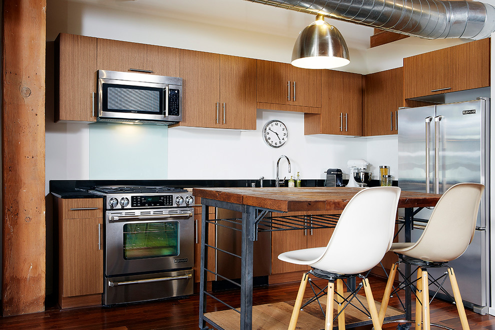 Aménagement d'une cuisine industrielle en bois brun avec un plan de travail en granite, un électroménager en acier inoxydable, parquet foncé, îlot et un placard à porte plane.