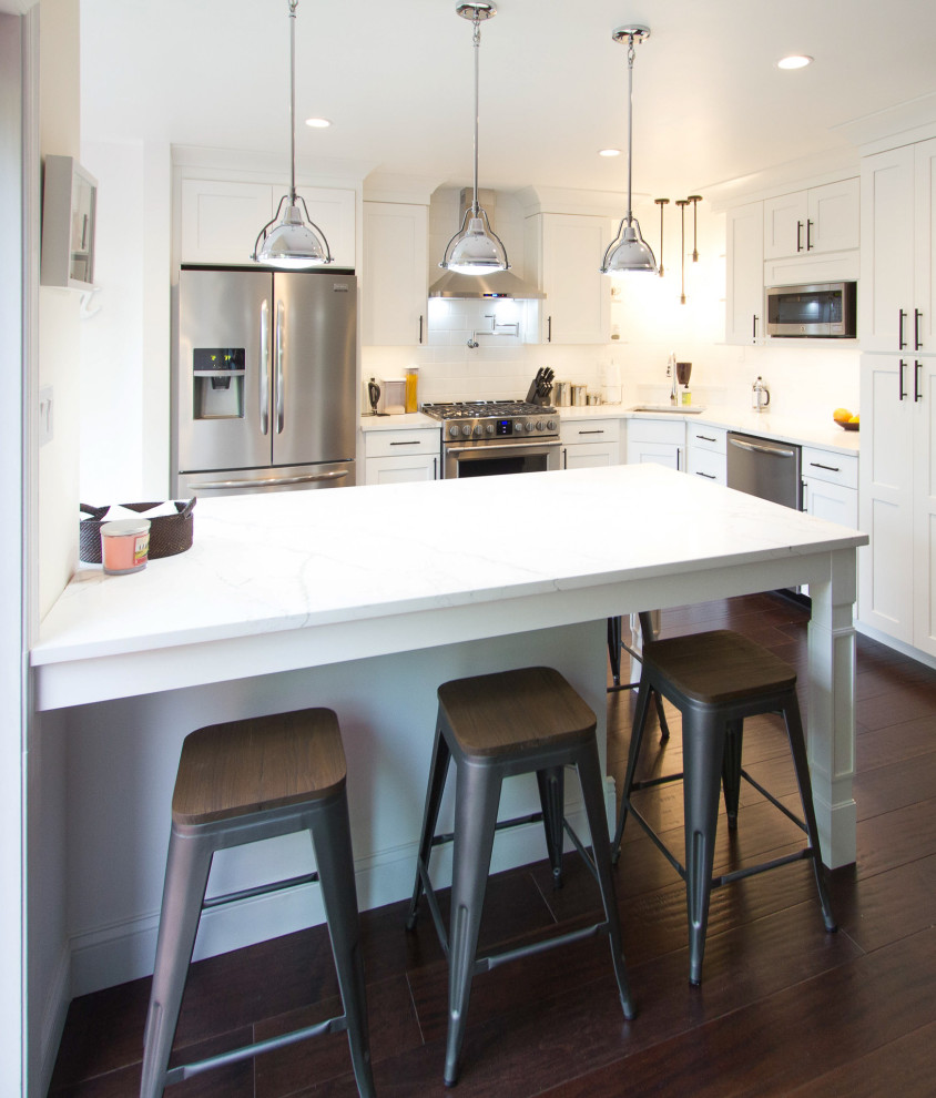 Mid-sized trendy l-shaped dark wood floor and brown floor open concept kitchen photo in Philadelphia with an undermount sink, recessed-panel cabinets, white cabinets, quartz countertops, white backsplash, subway tile backsplash, stainless steel appliances, an island and white countertops