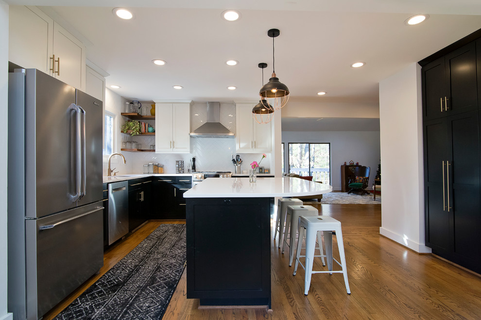 Photo of a medium sized industrial l-shaped kitchen/diner in Raleigh with a submerged sink, shaker cabinets, black cabinets, engineered stone countertops, white splashback, ceramic splashback, stainless steel appliances, medium hardwood flooring, an island, brown floors and white worktops.