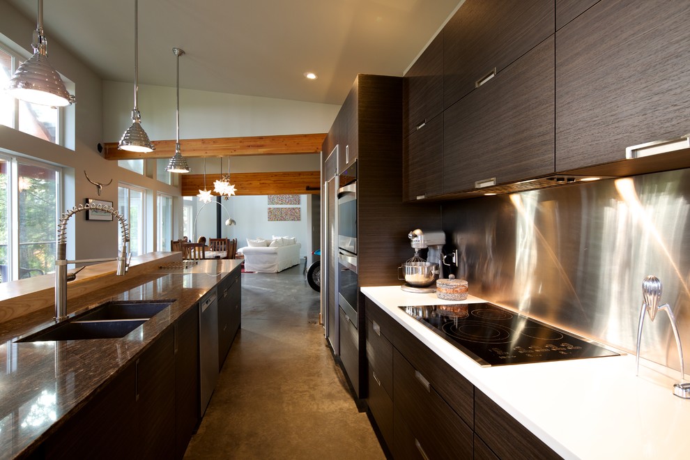 Large industrial galley open plan kitchen in Vancouver with a submerged sink, flat-panel cabinets, dark wood cabinets, quartz worktops, metallic splashback, stainless steel appliances, concrete flooring and an island.