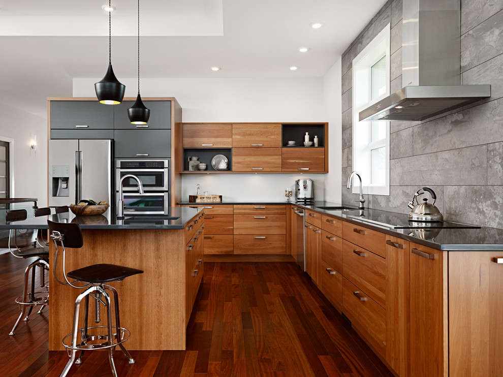 Bild på ett mellanstort funkis l-kök, med en undermonterad diskho, släta luckor, skåp i mellenmörkt trä, bänkskiva i kvarts, grått stänkskydd, stänkskydd i keramik, rostfria vitvaror, mellanmörkt trägolv och en köksö