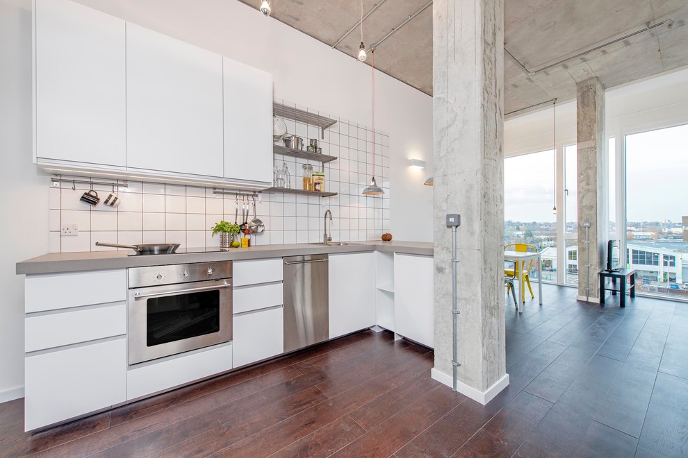 Foto på ett industriellt kök med öppen planlösning, med bänkskiva i betong, släta luckor, vita skåp, vitt stänkskydd, rostfria vitvaror och en halv köksö