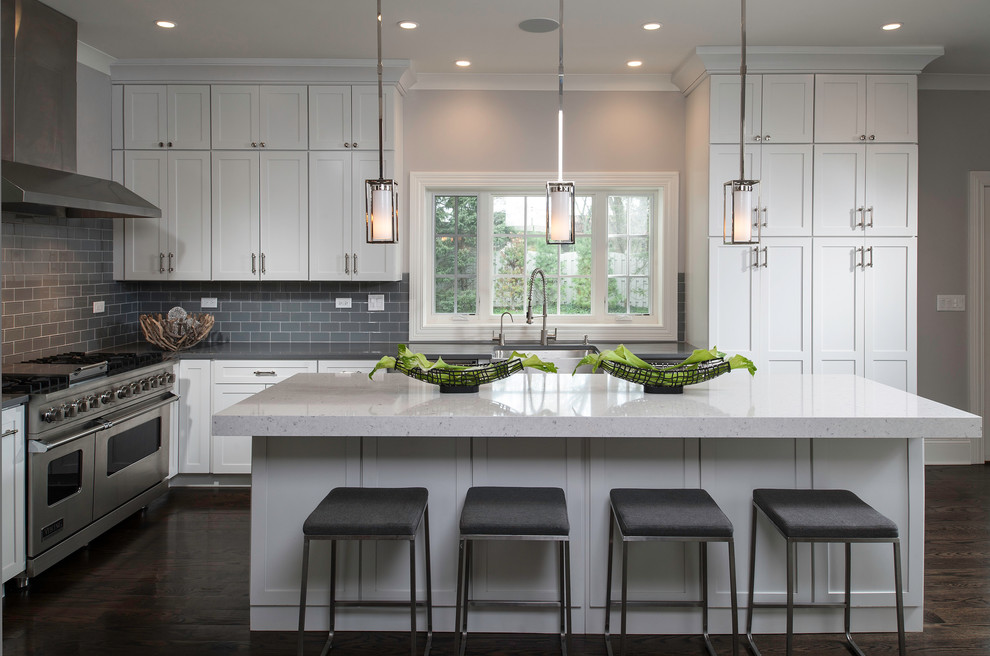 Inspiration for a transitional dark wood floor kitchen remodel in Chicago with a farmhouse sink, shaker cabinets, white cabinets, quartz countertops, gray backsplash, glass tile backsplash, stainless steel appliances and an island