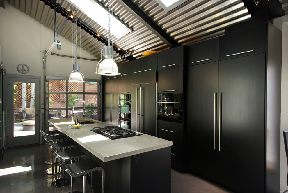 Urban galley kitchen photo in Salt Lake City with concrete countertops, a single-bowl sink, flat-panel cabinets, black cabinets and paneled appliances