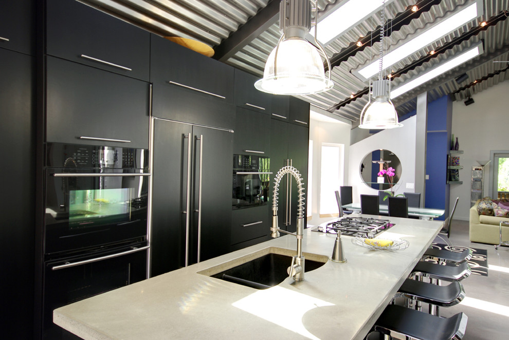 Стильный дизайн: кухня-гостиная в современном стиле с плоскими фасадами, черными фасадами, столешницей из бетона и черной техникой - последний тренд