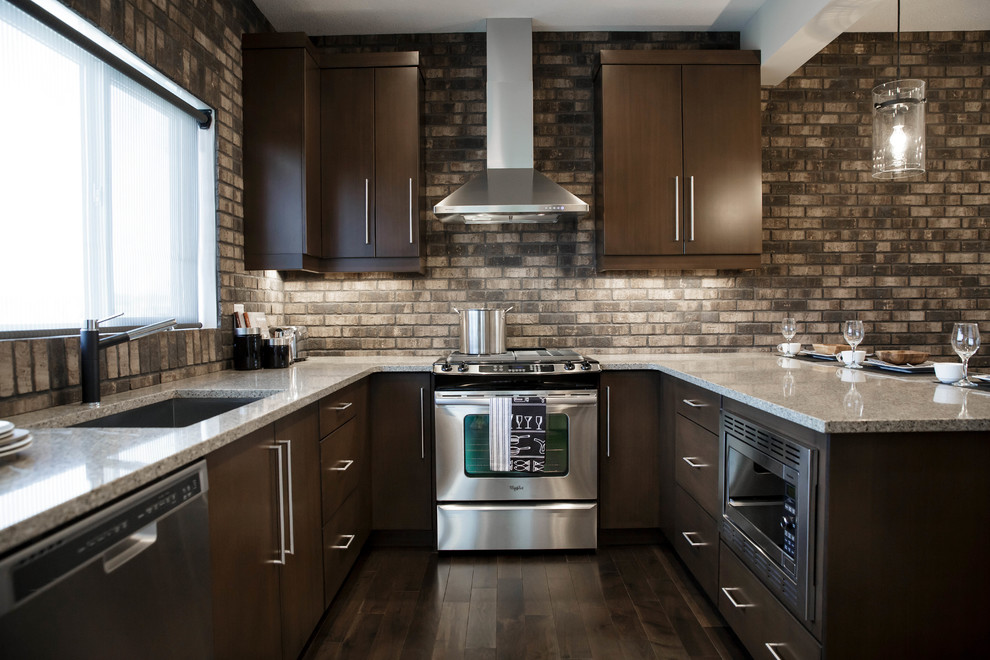 Inspiration for a mid-sized industrial u-shaped medium tone wood floor and brown floor eat-in kitchen remodel in Calgary with an undermount sink, flat-panel cabinets, medium tone wood cabinets, quartz countertops, brown backsplash, brick backsplash, stainless steel appliances and a peninsula