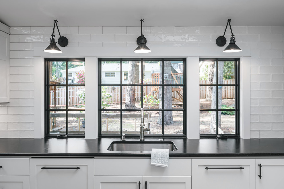 Exempel på ett stort lantligt svart svart kök, med en undermonterad diskho, luckor med infälld panel, vita skåp, bänkskiva i täljsten, vitt stänkskydd, stänkskydd i tunnelbanekakel, rostfria vitvaror, klinkergolv i porslin, en köksö och grått golv