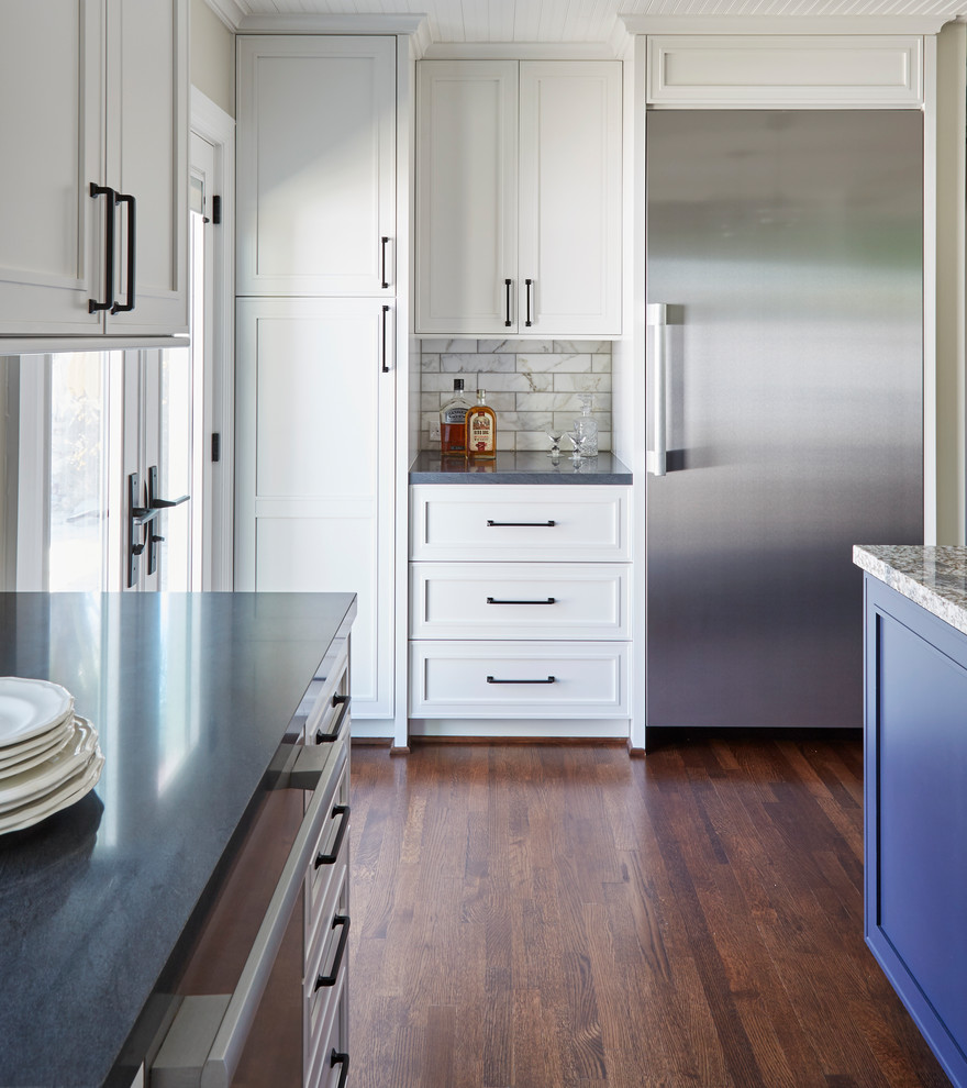Foto på ett mellanstort lantligt brun kök, med en rustik diskho, luckor med infälld panel, vita skåp, granitbänkskiva, vitt stänkskydd, stänkskydd i stenkakel, rostfria vitvaror, mörkt trägolv, en köksö och brunt golv