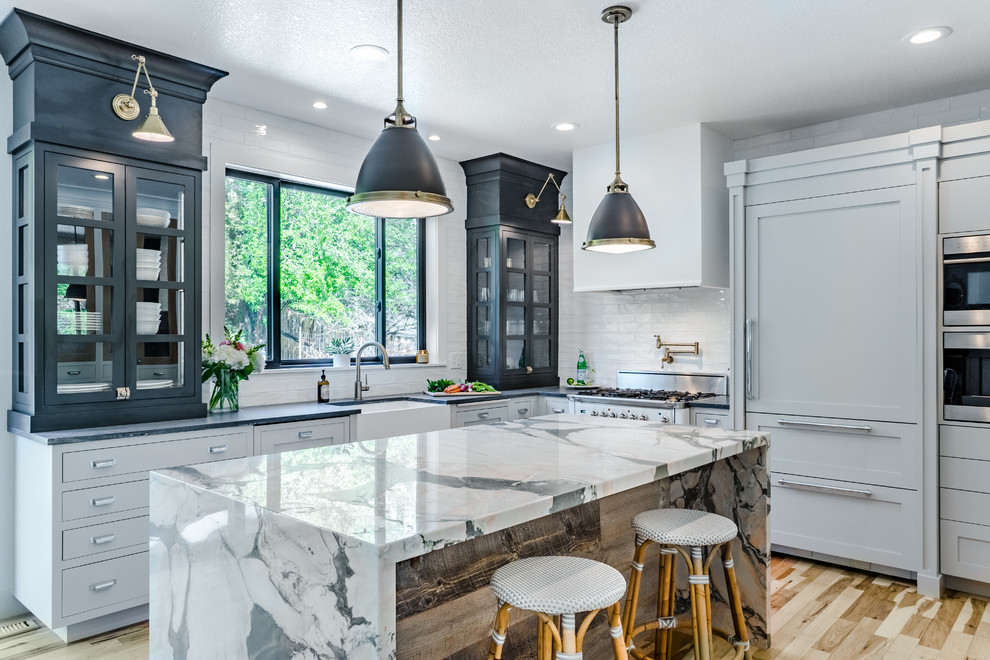 Exemple d'une cuisine encastrable chic de taille moyenne avec un évier de ferme, plan de travail en marbre, une crédence blanche, une crédence en céramique, îlot, un placard à porte vitrée, parquet clair, un sol beige et des portes de placard noires.