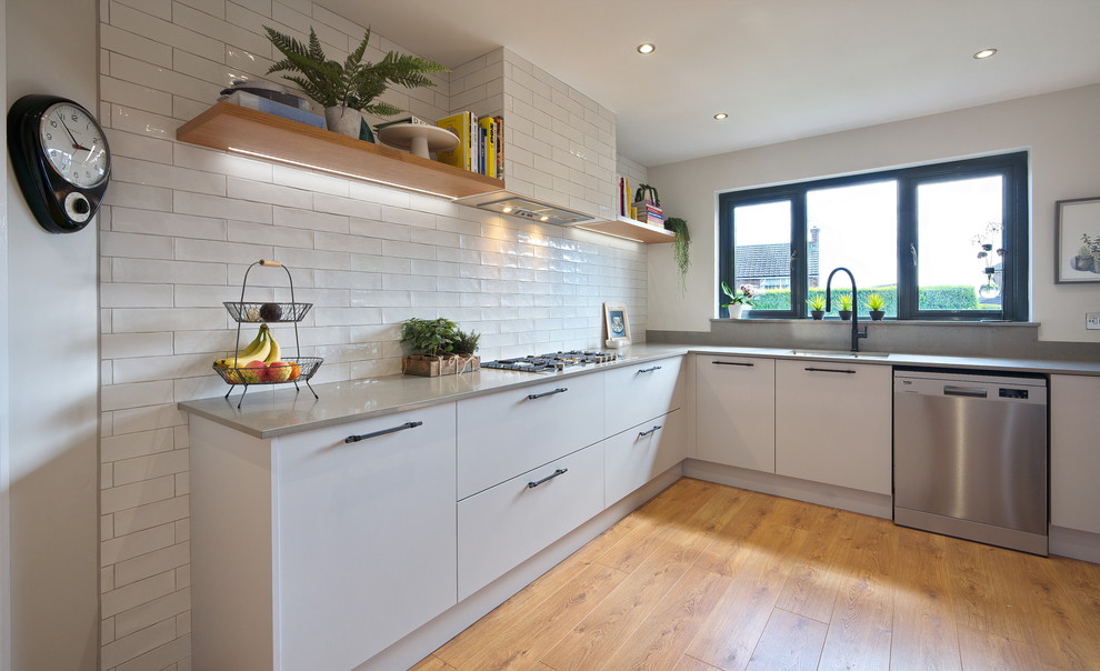 Design ideas for a medium sized urban l-shaped kitchen/diner in Other with a built-in sink, flat-panel cabinets, grey cabinets, quartz worktops, white splashback, ceramic splashback, stainless steel appliances, laminate floors, an island, brown floors and grey worktops.