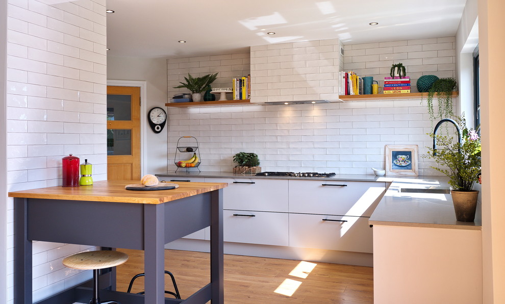 Medium sized contemporary l-shaped kitchen/diner in Other with flat-panel cabinets, quartz worktops, white splashback, ceramic splashback, laminate floors, an island, brown floors, grey worktops, a submerged sink and white cabinets.