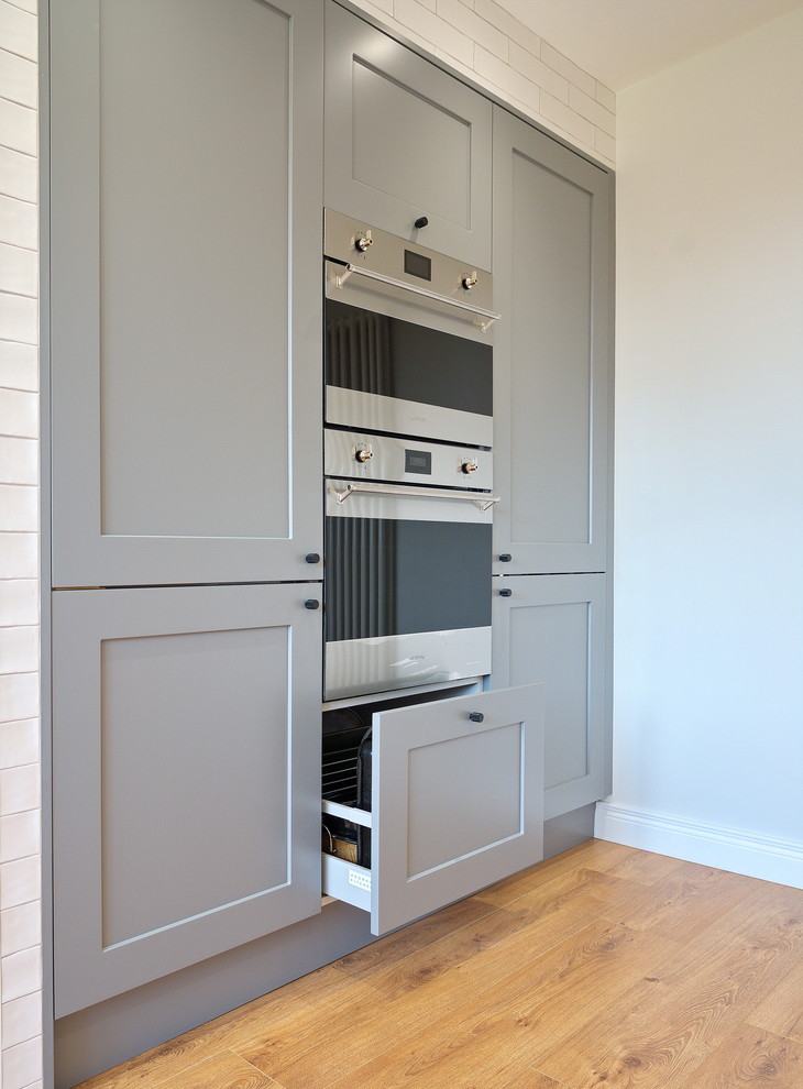 Medium sized urban l-shaped kitchen/diner in Other with a built-in sink, flat-panel cabinets, grey cabinets, quartz worktops, white splashback, ceramic splashback, stainless steel appliances, laminate floors, an island, brown floors and grey worktops.