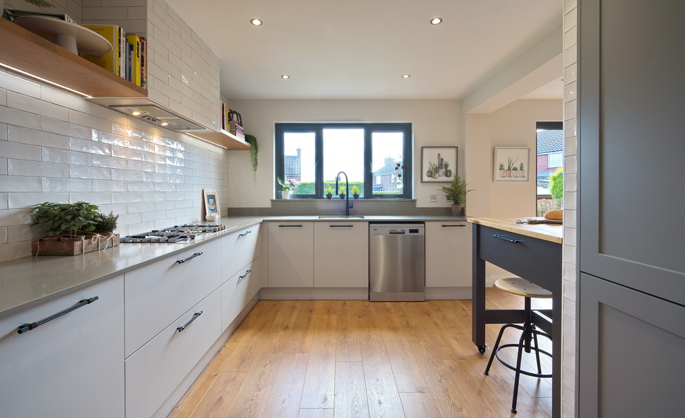 Photo of a medium sized urban l-shaped kitchen/diner in Other with a built-in sink, flat-panel cabinets, grey cabinets, quartz worktops, white splashback, ceramic splashback, stainless steel appliances, laminate floors, an island, brown floors and grey worktops.