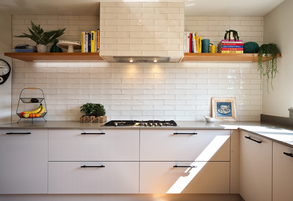 This is an example of a medium sized industrial l-shaped kitchen/diner in Other with a built-in sink, flat-panel cabinets, grey cabinets, quartz worktops, white splashback, ceramic splashback, stainless steel appliances, laminate floors, an island, brown floors and grey worktops.