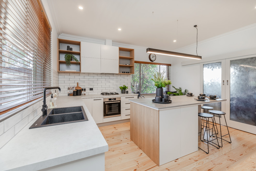 Inspiration for a large contemporary u-shaped kitchen/diner in Adelaide with a double-bowl sink, flat-panel cabinets, white cabinets, engineered stone countertops, white splashback, metro tiled splashback, black appliances, light hardwood flooring, an island, yellow floors and grey worktops.