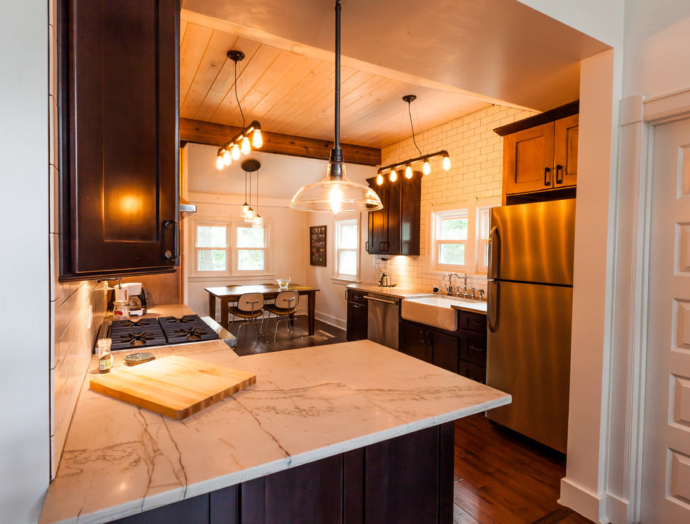 Example of a mid-sized urban galley dark wood floor eat-in kitchen design in Chicago with a farmhouse sink, shaker cabinets, dark wood cabinets, quartzite countertops, white backsplash, ceramic backsplash, stainless steel appliances and a peninsula