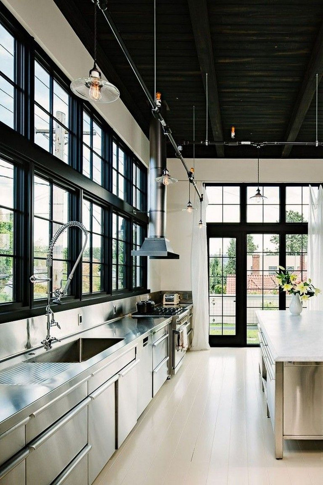 Foto på ett stort industriellt vit linjärt kök och matrum, med en integrerad diskho, släta luckor, skåp i rostfritt stål, bänkskiva i rostfritt stål, vitt stänkskydd, rostfria vitvaror, ljust trägolv, en köksö och brunt golv