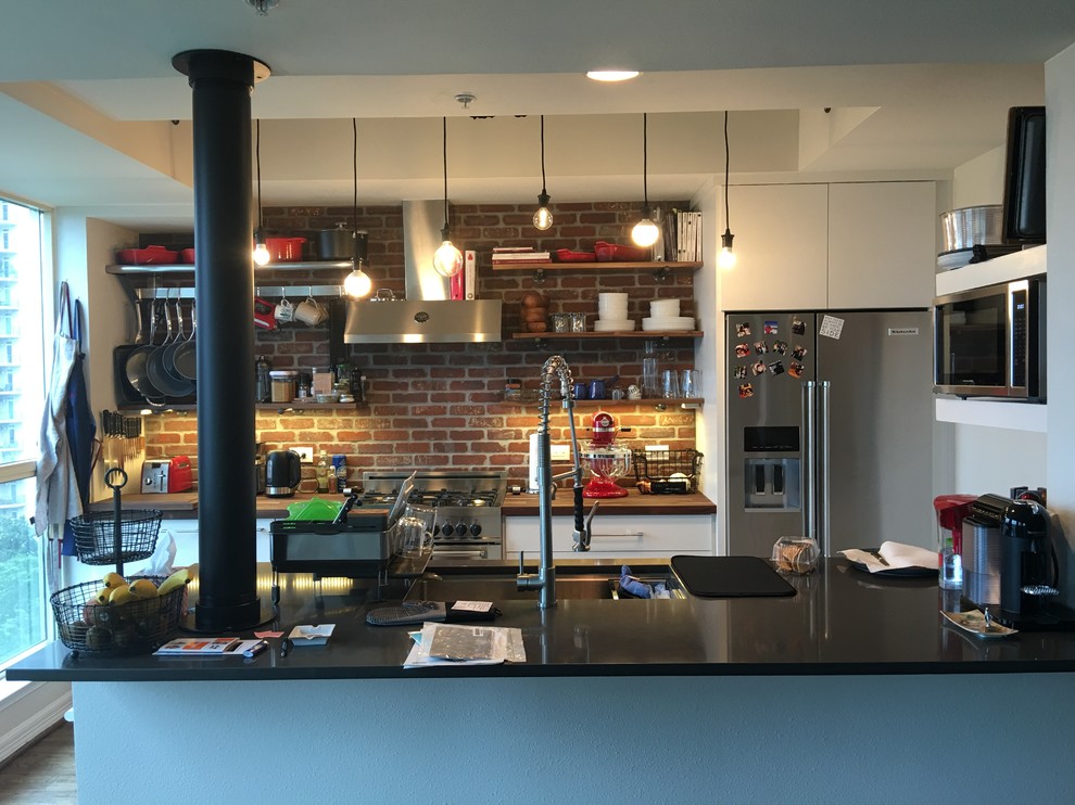 Foto på ett avskilt, mellanstort industriellt kök, med en undermonterad diskho, öppna hyllor, vita skåp, träbänkskiva, rött stänkskydd, stänkskydd i tegel, rostfria vitvaror och en köksö