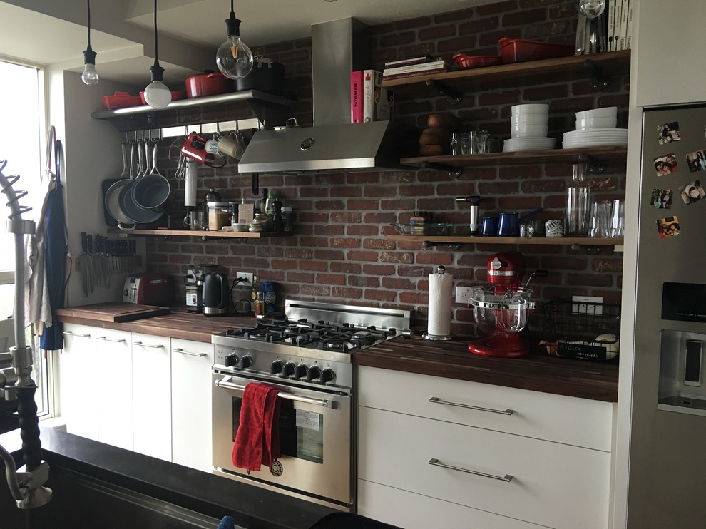 Industriell inredning av ett mellanstort, avskilt kök, med en undermonterad diskho, öppna hyllor, vita skåp, träbänkskiva, rött stänkskydd, stänkskydd i tegel, rostfria vitvaror och en köksö