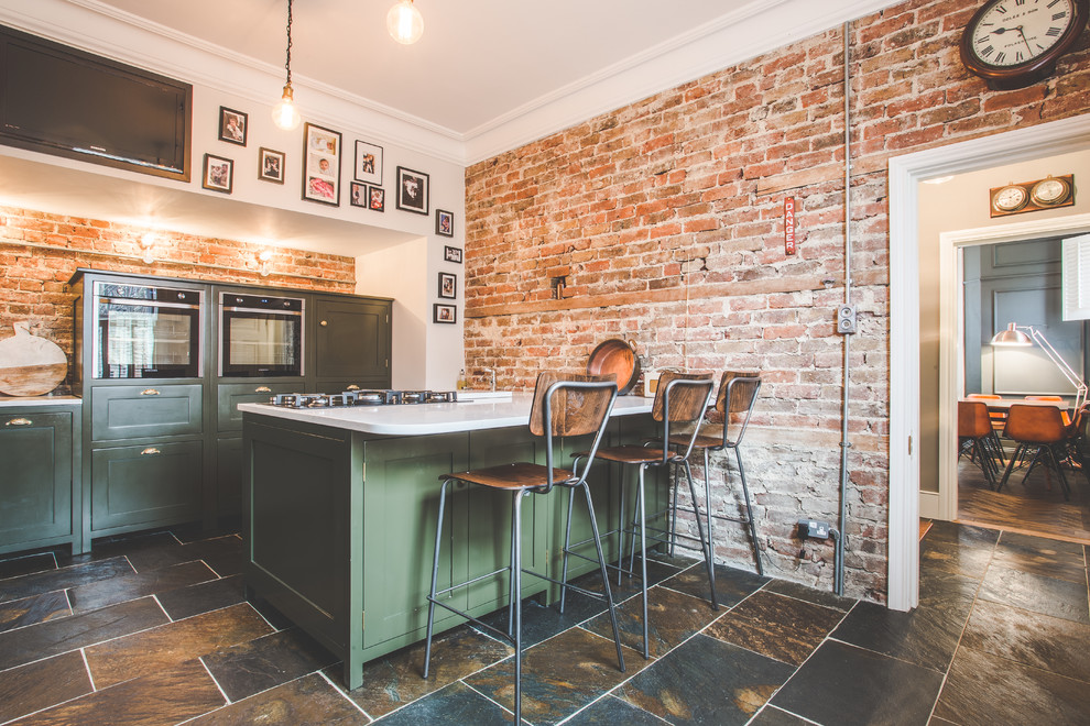 This is an example of a medium sized urban galley enclosed kitchen in Sussex with shaker cabinets, green cabinets, quartz worktops, slate flooring, white worktops, brown splashback, brick splashback, integrated appliances, a breakfast bar and brown floors.