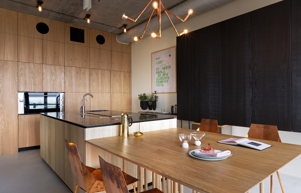 Réalisation d'une cuisine américaine urbaine en bois brun avec un placard à porte plane, îlot, un sol gris et plan de travail noir.