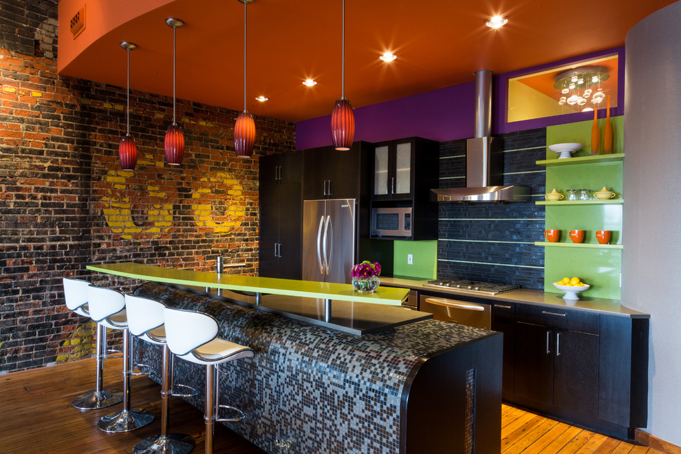 На фото: кухня в стиле лофт с плоскими фасадами, темными деревянными фасадами, разноцветным фартуком, техникой из нержавеющей стали, паркетным полом среднего тона и островом с