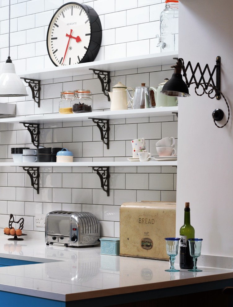 Foto på ett litet, avskilt industriellt l-kök, med en dubbel diskho, släta luckor, blå skåp, bänkskiva i kvarts, vitt stänkskydd, stänkskydd i tunnelbanekakel, svarta vitvaror, linoleumgolv och en halv köksö