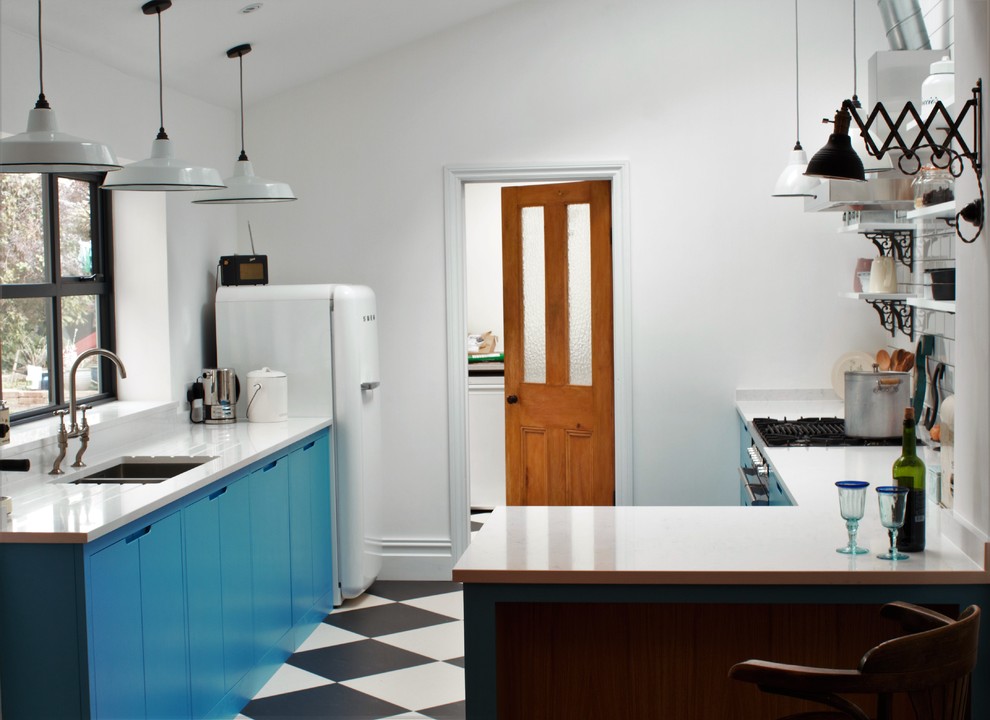 Photo of a small industrial l-shaped enclosed kitchen in Other with a double-bowl sink, flat-panel cabinets, blue cabinets, engineered stone countertops, white splashback, metro tiled splashback, black appliances, lino flooring and a breakfast bar.