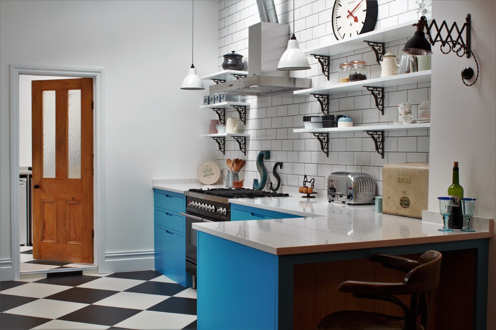 Foto på ett litet, avskilt industriellt l-kök, med en dubbel diskho, släta luckor, blå skåp, bänkskiva i kvarts, vitt stänkskydd, stänkskydd i tunnelbanekakel, svarta vitvaror, linoleumgolv och en halv köksö