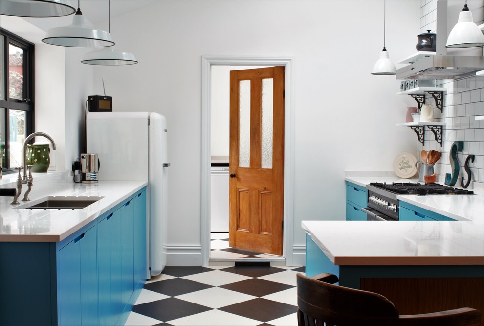 Photo of a small industrial l-shaped enclosed kitchen in Other with a double-bowl sink, flat-panel cabinets, blue cabinets, engineered stone countertops, white splashback, metro tiled splashback, black appliances, lino flooring and a breakfast bar.