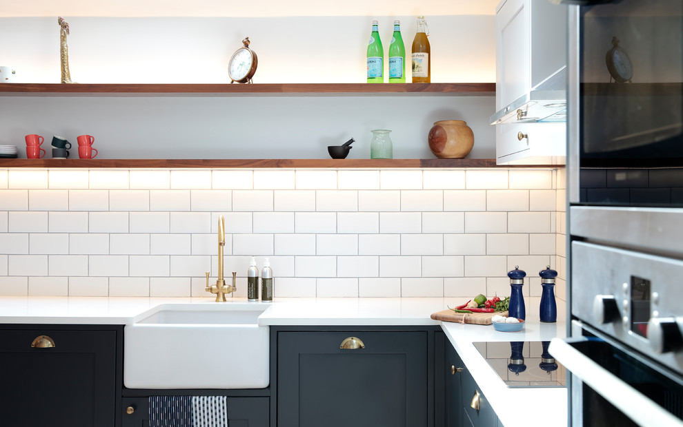 Inspiration for a medium sized urban l-shaped kitchen/diner in London with shaker cabinets, blue cabinets, white splashback, ceramic splashback, stainless steel appliances, a breakfast bar, beige floors and white worktops.
