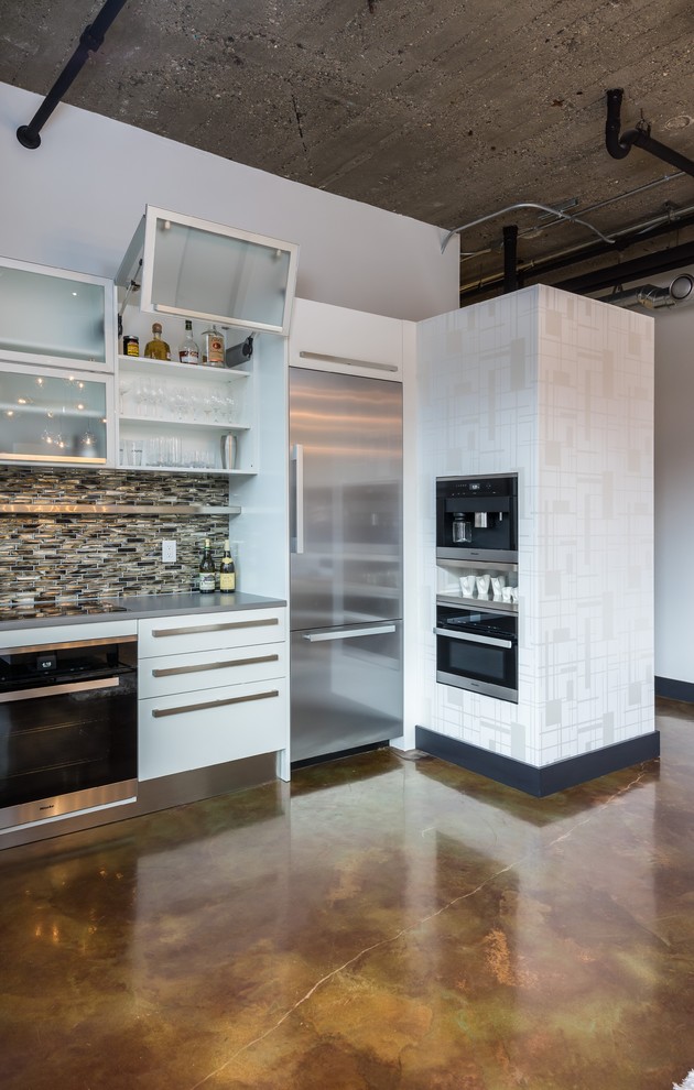 Inspiration for a mid-sized industrial u-shaped concrete floor and brown floor eat-in kitchen remodel in Detroit with an undermount sink, flat-panel cabinets, white cabinets, solid surface countertops, multicolored backsplash, glass tile backsplash, stainless steel appliances and no island