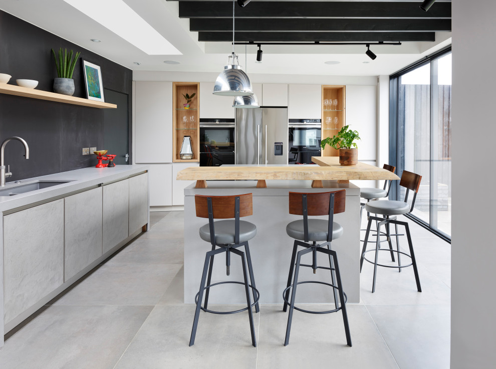 Urban eat-in kitchen photo in London with gray cabinets, concrete countertops, black appliances and an island