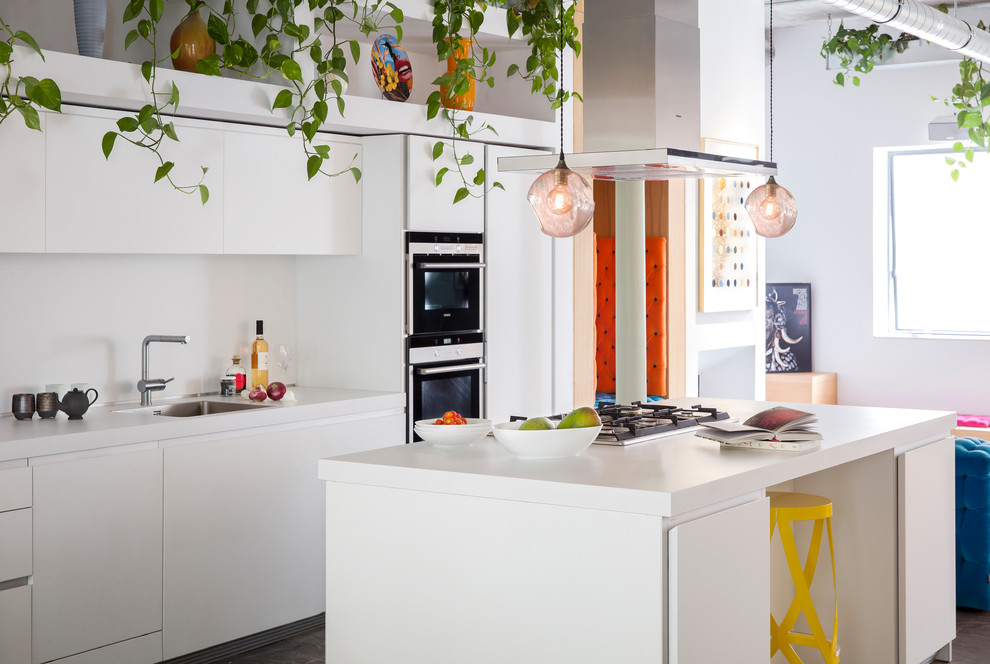 Photo of an eclectic galley open plan kitchen in London with a submerged sink, flat-panel cabinets, white cabinets, composite countertops, stainless steel appliances and an island.