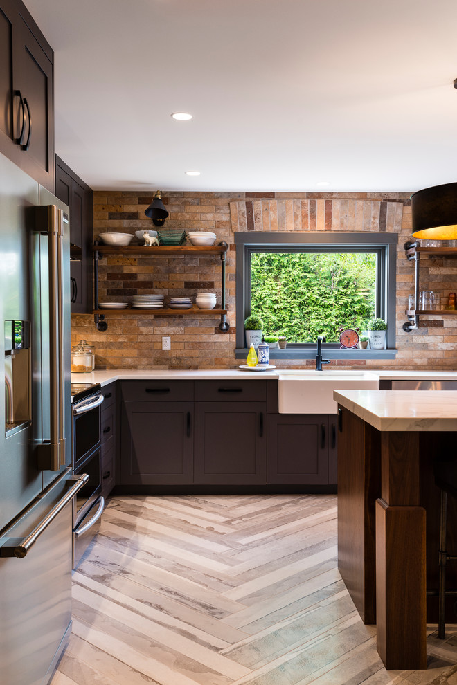 Photo of a large industrial l-shaped open plan kitchen in Vancouver with a submerged sink, shaker cabinets, grey cabinets, engineered stone countertops, brown splashback, brick splashback, stainless steel appliances, porcelain flooring, an island and beige floors.