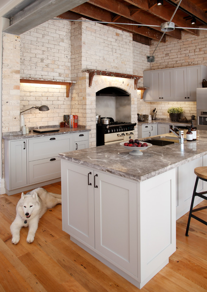 Immagine di una cucina industriale con lavello sottopiano, ante grigie, top in marmo, paraspruzzi beige, elettrodomestici in acciaio inossidabile e pavimento in legno massello medio