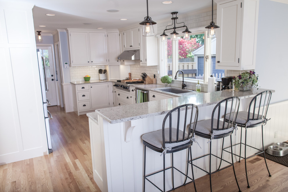 Medium sized urban l-shaped open plan kitchen in Grand Rapids with a submerged sink, recessed-panel cabinets, white cabinets, engineered stone countertops, white splashback, ceramic splashback, stainless steel appliances, light hardwood flooring and no island.