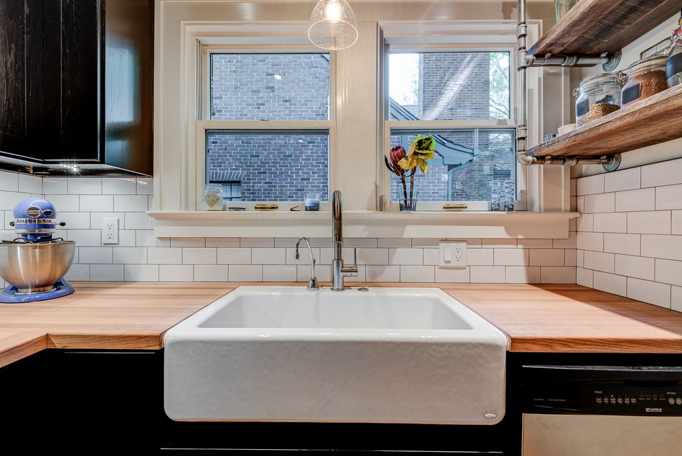 Photo of a small urban u-shaped kitchen/diner in Chicago with a belfast sink, shaker cabinets, black cabinets, wood worktops, white splashback, stainless steel appliances, light hardwood flooring, a breakfast bar and metro tiled splashback.